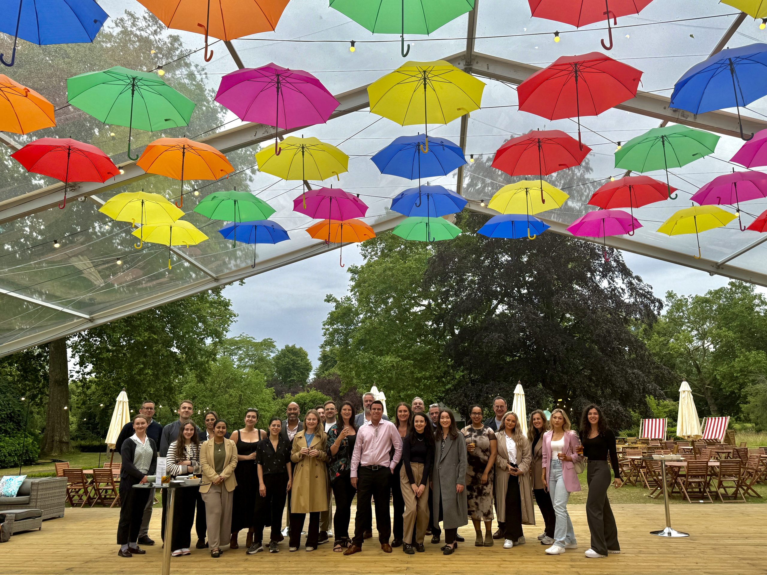 Group of event professionals smiling under a canopy with colourful umbrellas above them.